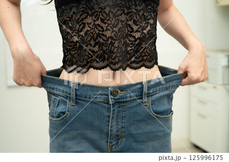 Young Asian woman losing weight wearing loose pants in oversize jeans. 125996175