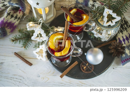 Mulled wine with orange and spices, Christmas decor and burning candles, on a white wooden table against the background of winter nature. Mulled wine with orange and spices, Christmas decor and burning candles, on a white wooden table against the background of winter nature. 125996209