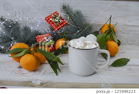 Cup of hot chocolate with marshmallows, tangerines and Christmas decorations on white wooden background. Cup of hot chocolate with marshmallows, tangerines and Christmas decorations on white wooden background. 125996223