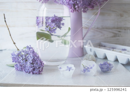 Lilac flowers, ice cubes and a glass of water on a light background and lilac flowers in a vase Lilac flowers, ice cubes and a glass of water on a light background and lilac flowers in a vase 125996241