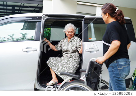 Caregiver help Asian elderly woman disability patient get in her car. Caregiver help Asian elderly woman disability patient get in her car. 125996298