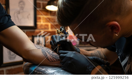 Tattoo Artist Concentrating on Intricate Arm Tattoo in Studio Tattoo Artist Concentrating on Intricate Arm Tattoo in Studio 125999256