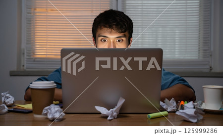Freelancer Surrounded by Coffee Cups and Crumpled Papers in Dim Apartment Freelancer Surrounded by Coffee Cups and Crumpled Papers in Dim Apartment 125999286