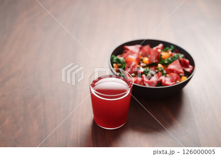 Salad with kale, bresaola and cherry tomatoes decorated with capers in black bowl and glass of red drink on walnut wood table 126000005