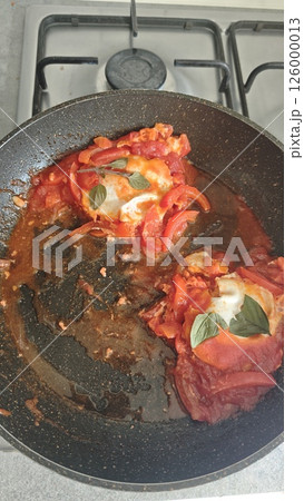 Shakshuka with poached eggs in tomato and pepper sauce cooked in a skillet on stovetop. Concept of Middle Eastern cuisine, rustic home cooking and vegetarian meal 126000013