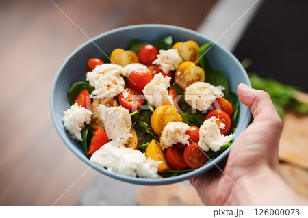 amn hand hold salad with red and yellow cherry tomatoes , mozzarella and spinach in blue bowl 126000073