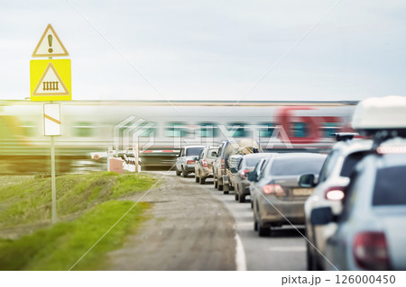 A queue of cars is waiting for a passenger train to travel at a railway crossing outside the city. The automatic barrier prevents unauthorized access to the railway track and ensures trouble-free A queue of cars is waiting for a passenger train to travel at a railway crossing outside the city. The automatic barrier prevents unauthorized access to the railway track and ensures trouble-free 126000450