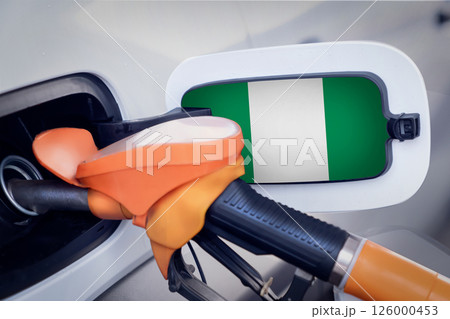 The Nigeria flag on the lid of the gas tank of a car at a gas station in close-up. High or low gasoline prices at Nigerian gas stations. In Nigeria, gasoline prices are rising due to a shortage of 126000453