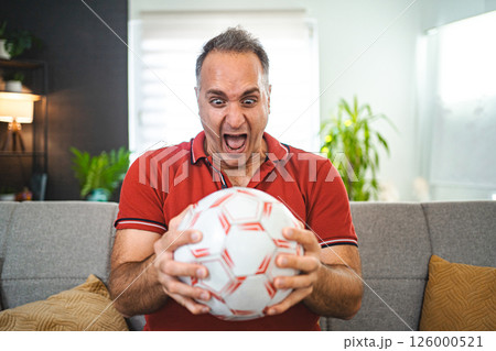 Excited middle aged man watching soccer game at home Excited middle aged man watching soccer game at home 126000521