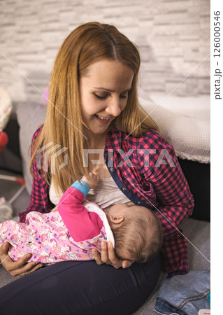 Mother breastfeeding her baby at home in a cozy living room 126000546