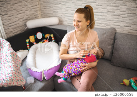 Mother breastfeeding her baby on a cozy couch during daytime at home 126000559