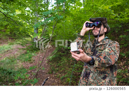 Soldier exploring forest using binoculars and compass for navigation 126000565