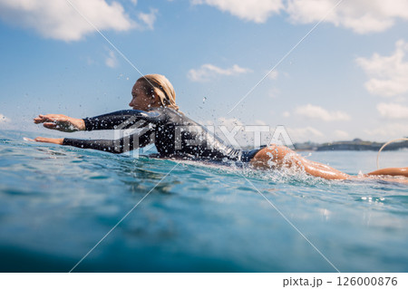 Beautiful woman surfer paddling on surfboard through crystal clear water Beautiful woman surfer paddling on surfboard through crystal clear water 126000876