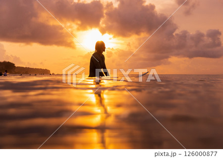 Surfer waiting for a wave at golden sunset, reflecting peaceful vibes and ocean adventure moments 126000877