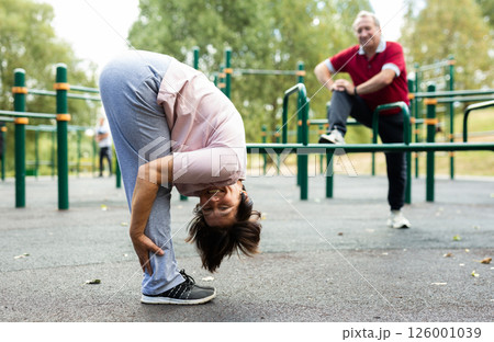 Mature woman doing yoga outdoors in city sports ground 126001039