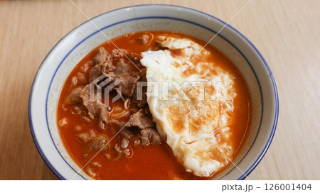 close up of tomato soup noodles with a pan fried egg and beef slice in a bowl with copy space 126001404