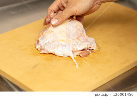 鳥のもも肉を合成ゴムのまな板の上で調理している 126001456
