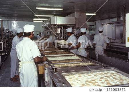Industrial bakery operation: workers in uniform managing dough production in a modern facility 126003871