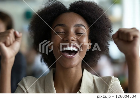 Joyful celebration of success with cheerful young woman expressing excitement and happiness in bright modern setting 126004334