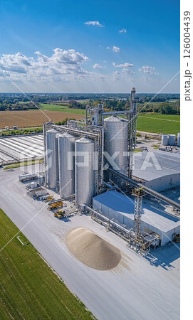 Modern agricultural storage facility with grain silos under blue sky in rural landscape Modern agricultural storage facility with grain silos under blue sky in rural landscape 126004439