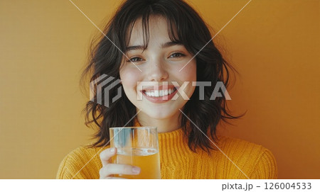 Cheerful woman enjoying refreshing beverage against vibrant orange backdrop for lifestyle and wellness themes 126004533