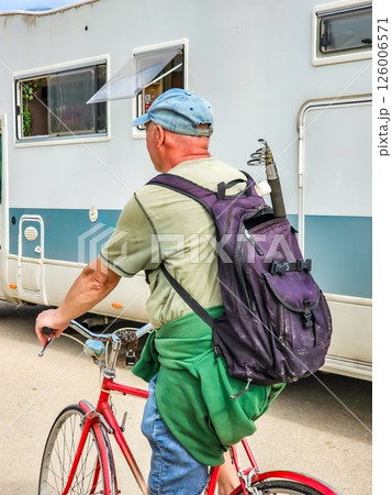 Man Riding Bicycle to Go Fishing with a Fishing Rod Attached to His Backpack 126006571