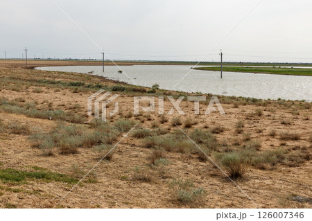 Flat arid landscape with water and power lines stretching across Kazakhstan 126007346