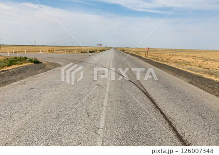 Straight asphalt road stretches through flat arid landscape in Atyrau Region Kazakhstan Straight asphalt road stretches through flat arid landscape in Atyrau Region Kazakhstan 126007348
