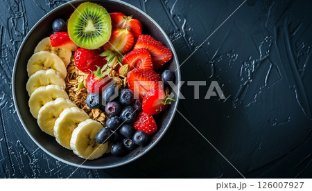 A round plate of granola and mixed fruits on a black table, with copy space 126007927