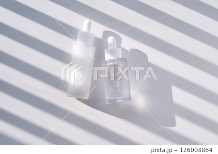 Two serums with peptides and Spicule Ampoule serum on a white background with stripes of shadows. Two serums with peptides and Spicule Ampoule serum on a white background with stripes of shadows. 126008864