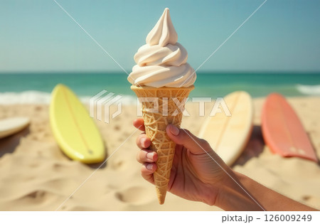 Hand holding ice cream in cone with sea and surfboards in the background 126009249
