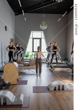 Young caucasian women exercising on pilates reformers in a bright studio. Their workout focuses on core strength and flexibility in a modern fitness environment. 126009534