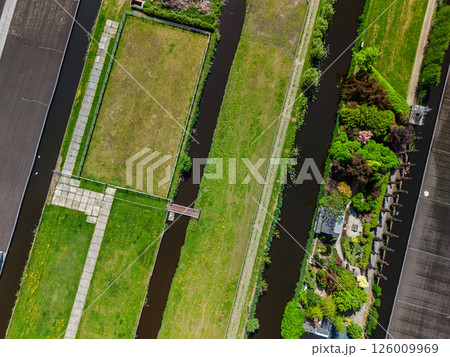 Aerial view of a lush countryside garden surrounded by canals and farmlands, with a cozy house and colorful trees, set in a peaceful rural landscape under a clear blue sky. Aerial view of a lush countryside garden surrounded by canals and farmlands, with a cozy house and colorful trees, set in a peaceful rural landscape under a clear blue sky. 126009969