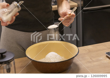 Woman adding ingredients together to prepare dough 126009995