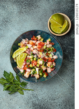 Peruvian seafood ceviche with shrimps, octopus, tomatoes, cucumber, and parsley in a bowl served with lime top view 126010174