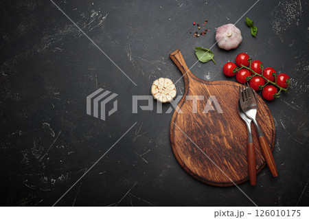 Food background with fresh vegetables, cooking ingredients, spices resting on rustic wooden cutting board, black background, space for text 126010175