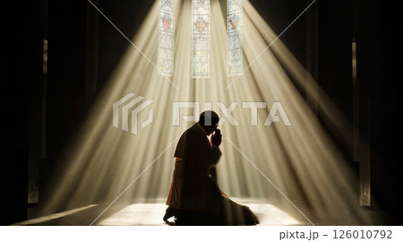 A silhouette of the Pope kneeling in prayer inside a vast, dimly lit cathedral. 126010792