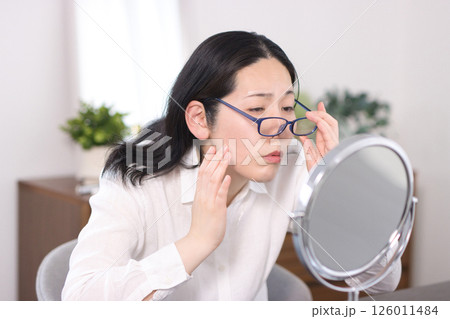 老眼鏡をかけて鏡に映る小じわやしみを見るミドル女性 老眼鏡をかけて鏡に映る小じわやしみを見るミドル女性 126011484