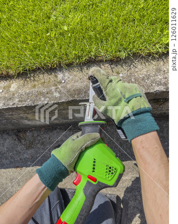 Male hands in gloves cut metal bolt protruding from concrete beam with an electric reciprocating saw. Male hands in gloves cut metal bolt protruding from concrete beam with an electric reciprocating saw. 126011629