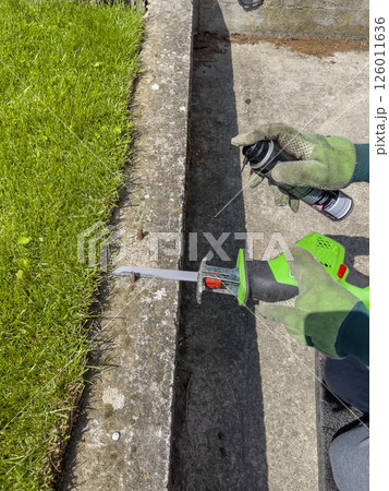 Male hands in green gloves cut a metal bolt protruding from a concrete beam with an electric reciprocating saw 126011636