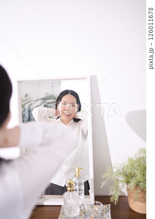 鏡を見ながらネックレスを付ける笑顔のミドル女性 126011678