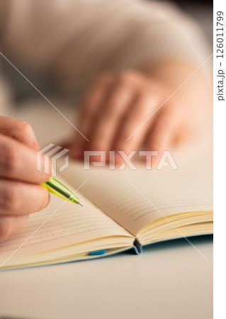 Close up image of human holding pen and writing something on blank white page in notebook. 126011799
