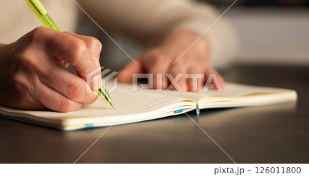 Side view of hand writing notes with pen in plain notebook. Minimalist workspace with natural lighting. 126011800