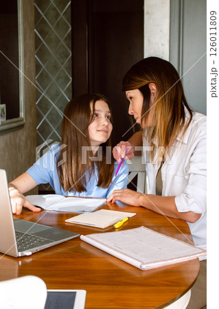 Family digital leisure time. Caucasian mother and daughter using laptop doing online activities, surfing internet, making video call in home interior. 126011809