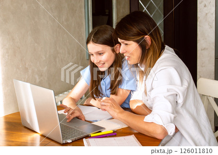 Family digital leisure time. Caucasian mother and daughter using laptop doing online activities, surfing internet, making video call in home interior. 126011810
