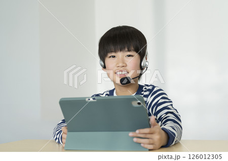 ヘッドセットをつけてタブレットPCに向かう小学4年生の男の子　カメラ目線で笑顔のポートレート 126012305