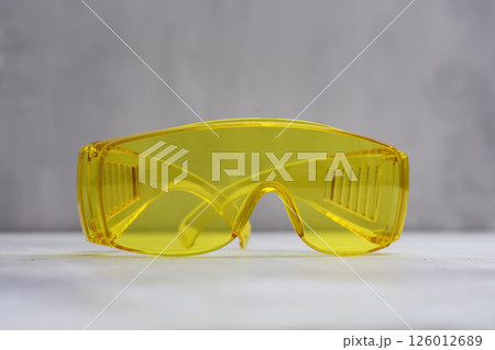 Bright yellow safety glasses placed on a light marble surface. Tool for eye protection during construction, laboratory work, or industrial tasks. 126012689