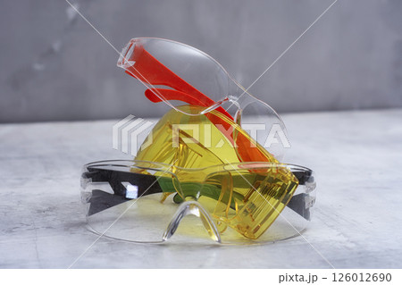 Set of protective safety glasses on a marble surface. Bright yellow lenses and clear lenses with red and green details. Concept for safety eye protection gear, and personal protective equipment. Set of protective safety glasses on a marble surface. Bright yellow lenses and clear lenses with red and green details. Concept for safety eye protection gear, and personal protective equipment. 126012690