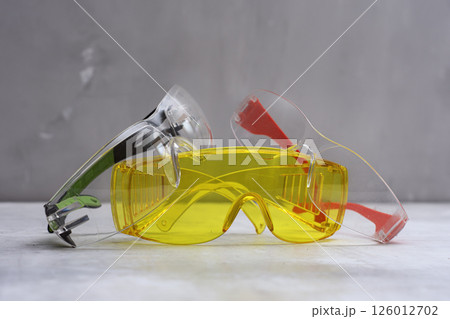 Set of protective safety glasses on a marble surface. Bright yellow lenses and clear lenses with red and green details. Concept for safety eye protection gear, and personal protective equipment. 126012702
