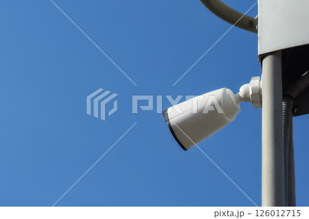 Outdoor CCTV camera on a metal pole against a clear blue sky. Outdoor CCTV camera on a metal pole against a clear blue sky. 126012715